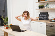 © Юлия Буракова - Portrait of a beautiful young woman with a laptop. Girl sitting at table in kitchen with laptop computer in white t-shirt