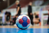 Handball ball on court' s floor. Blurred referees, coaches and athletes and field background.