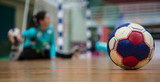 Handball ball on court floor. Blurred female goalkeeper background. Space for text, close up view.