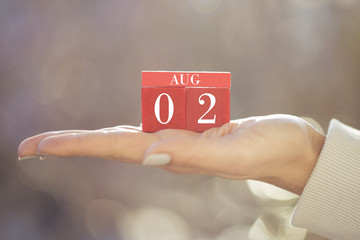 the woman is holding a red wooden calendar. Red wooden cube shape calendar for AUG 2 with hand 