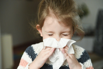 Sick little girl blowing her nose and covering it with handkerchief with eyes closed
