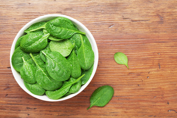 Wall Mural - Spinach leaves with water drops in bowl on wooden table top view. Healthy food.