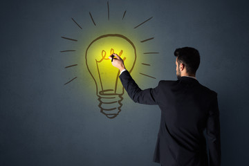 Canvas Print - Young businessman in black suit standing in front of a drawn yellow lightbulb 