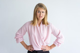 Portrait of young Caucasian businesswoman wearing pink blouse standing with hands on waist displeased at some rude behavior. Irritation, misunderstanding concept