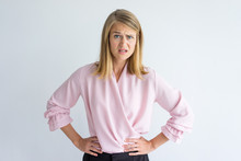 Portrait Of Young Caucasian Businesswoman Wearing Pink Blouse Standing With Hands On Waist Displeased At Some Rude Behavior. Irritation, Misunderstanding Concept