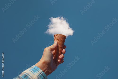 Fotografie, Obraz hand holding a sugar cone in front of a fluffy white cloud toned with a retro vi