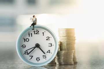 Reading,  Time and Business concept. Businessman miniature figures siting and reading a newspaper on vintage round clock with stack of coins.