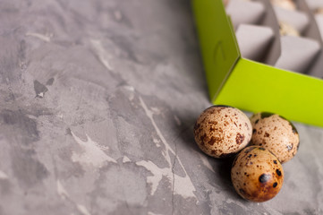 Poster - One green rectangle cardboard box with lot of spotted fresh quail eggs and scattered three eggs on old broken worn gray cement floor with copy space