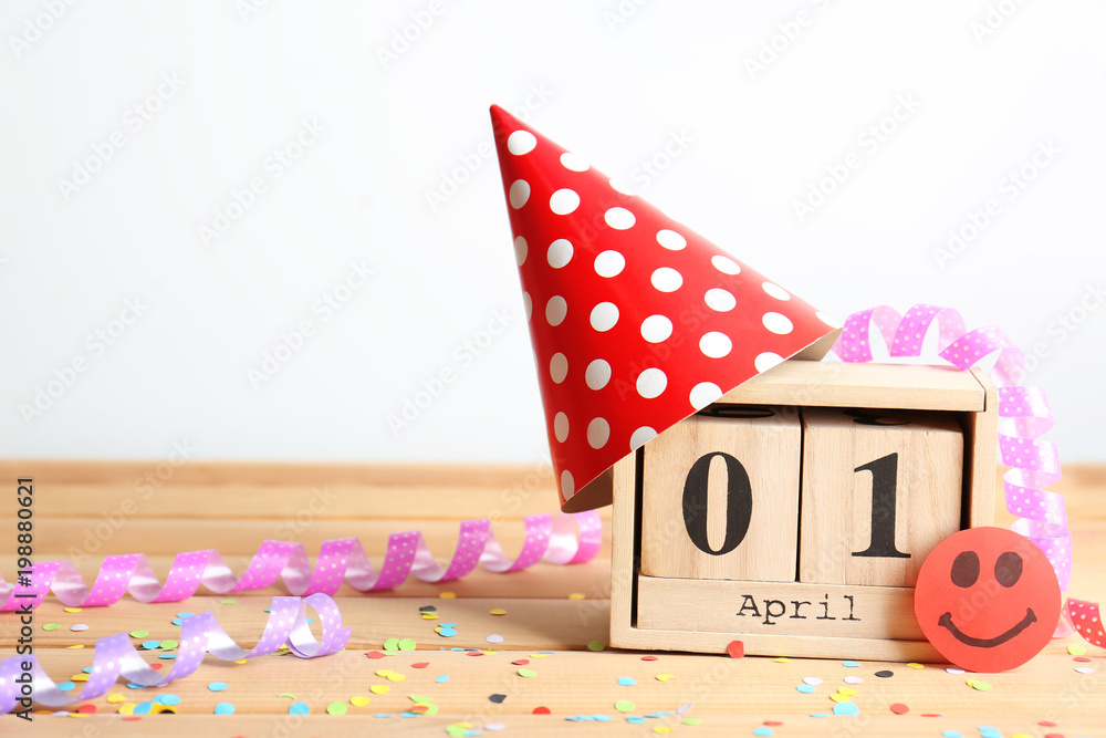Block calendar, party cap and confetti on table. April fool's day celebration