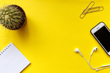 Modern workspace smartphone, notebook, headphones on yellow color background. Top view. Flat lay style.