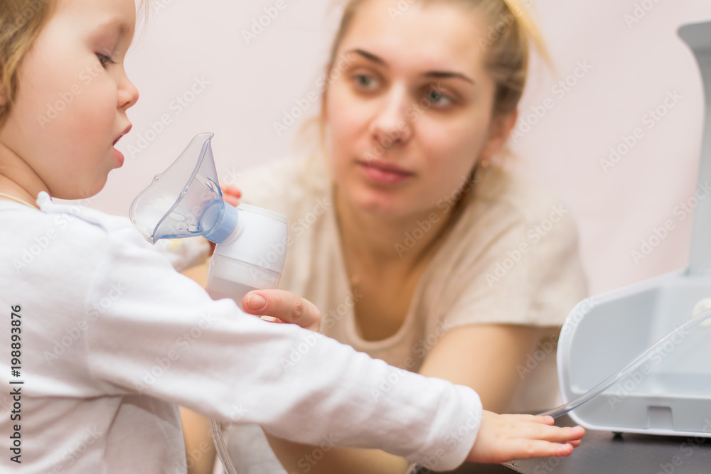 Two year old baby girl inhaling from the inhaler, her mother holding ...