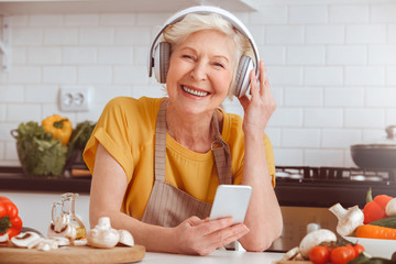 Older woman cooking, listen to music in mobile, toothy smiling