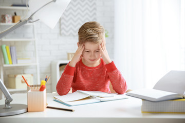 Wall Mural - Little boy suffering from headache while doing homework at table indoors