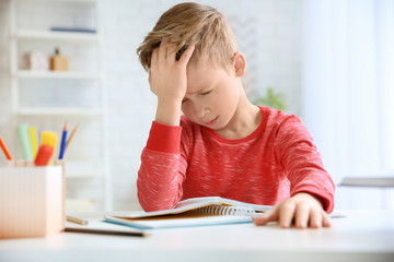 Wall Mural - Little boy suffering from headache while doing homework at table indoors