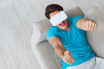 Young man wearing VR glasses relaxing on couch sofa