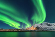 Aurora borealis. Lofoten islands, Norway. Aurora. Green northern lights. Starry sky with polar lights. Night winter landscape with aurora, sea with sky reflection and snowy mountains. Nature. Travel