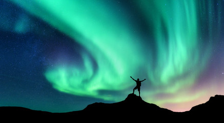 Wall Mural - aurora and silhouette of standing man with raised up arms on the mountain in norway. aurora borealis