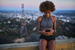 © Joshua Resnick - athletic african american woman using smartphone at runyon canyon while resting on bench at dusk