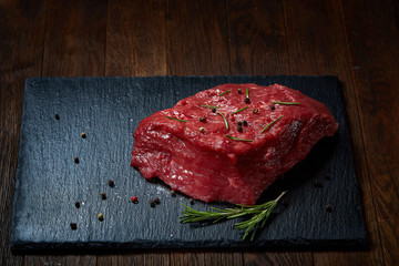 Wall Mural - Raw meat beef steaks on black slate board with spices and rosemary over wooden background, copy space