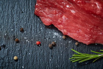 Wall Mural - Raw meat beef steaks on black slate board with spices and rosemary, selective focus, shallow depth of field