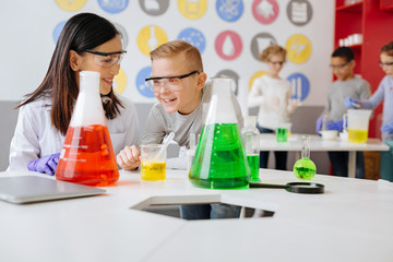 Wall Mural - Upbeat ambience. Cheerful young chemistry teacher and her student sitting at the table in the lab and laughing while discussing a chemical experiment