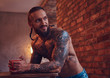 © Fxquadro - A handsome bearded tattoed male with a stylish haircut and muscular body, drinks coffee, leaning on a table.