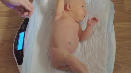 mother putting the newborn baby daughter on electronic scales, checking the weight and taking child.