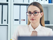 © cameravit - Portrait of young serious businesswoman looking at the camera while using laptop in office.