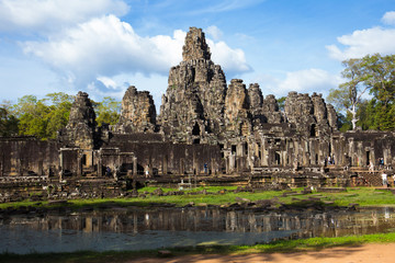 ancient public temple with tourist walk around and small lake infront with blue sky in cambodia