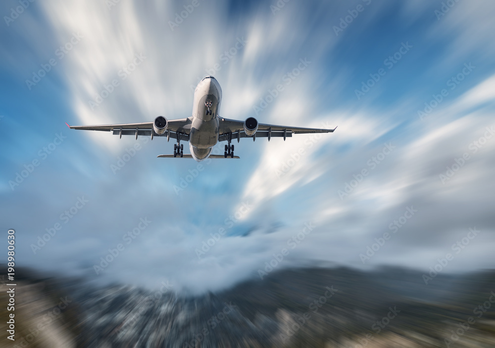 Big airplane mith motion blur effect at sunny bright day. Landscape with passenger airplane, blurred clouds, mountains, blue sky. Passenger aircraft in motion. Business travel. Commercial aircraft - obrazy, fototapety, plakaty 