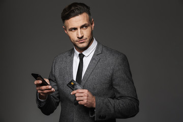Wall Mural - photo of confident successful man in suit and tie holding cell phone and credit card, isolated over 