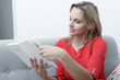 blond woman sitting in  sofa reading a book