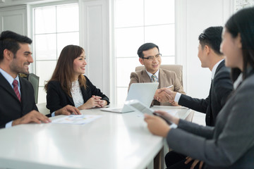 A confident business team of mixed ages and ethnicity are holding a meeting in a modern office. They are discussing ideas for their business development. Business partners shaking hand after complete 