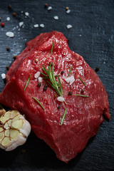 Wall Mural - Raw meat beef steaks on black slate board with spices, garlic and rosemary over wooden background, selective focus