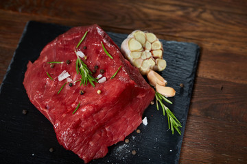 Wall Mural - Raw meat beef steaks on black slate board with spices, garlic and rosemary over wooden background, selective focus