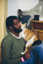 Man With Black Beard And Dark Skin Sitting At Home With White-orange Funny Cat