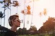 © Annatamila - Profile portrait of young female with short hair wearing sunglasses with palm trees on background