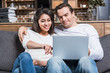 © LIGHTFIELD STUDIOS - happy multiethnic couple using laptop together on couch