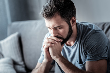 what to do. serious cheerless unhappy man holding his chin and looking down while thinking what to d