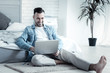 © Viacheslav Yakobchuk - Comfortable position. Positive happy joyful man sitting on the floor and looking at the laptop screen while feeling comfortable at home
