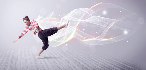 A beautiful young hip hop dancer dancing contemporary urban street dance in front of grey wall background with smokey lines and glitter concept.