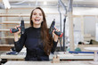 © Rithor - Portrait of cheerful young woman working in carpenters shop drilling holes in piece of wood while making furniture, copy space. Place for the text.