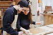 © Rithor - young happy family standing at a work bench in a carpentry workshop, process a tree a varnish. Family business. startup business. young specialist designer.