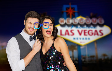 Poster - entertainment, luxury and fun concept - happy couple posing with party glasses over welcome to fabulous las vegas sign background