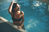 Fototapeta  - Young slim woman relaxing by swimming pool