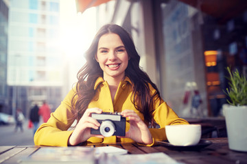 Wall Mural - travel, tourism, photography, leisure and people concept - happy young tourist woman or teenage girl with film camera and guidebook drinking cocoa at city street cafe terrace