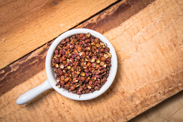 Poster - Exotic spices concept organic Chinese pepper, Sichuan pepper in white cup on wood background with copy space