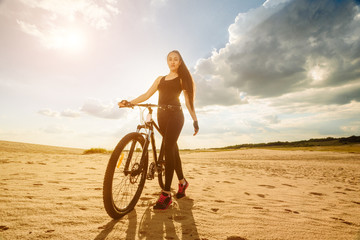 Wall Mural - Bicyclist the summer sunset on the desert road in the reserve territory. Full length image of young female cyclist. Summer sunset. Bicycle and ecology lifestyle concept.