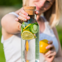 Wall Mural - healthy eating, drinks, diet. The girl is holding a detox drink from a lemon and mint with a cucumber on a background of green grass