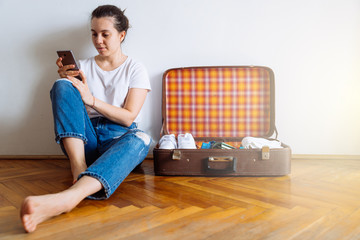 woman sit on floor with cellphone. packing clothes for trip. tra